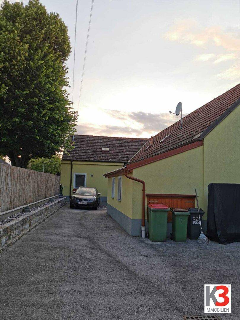Die Einfahrt zum Haus mit Mülltonnen und Blick auf die Rückseite des Gebäudes.