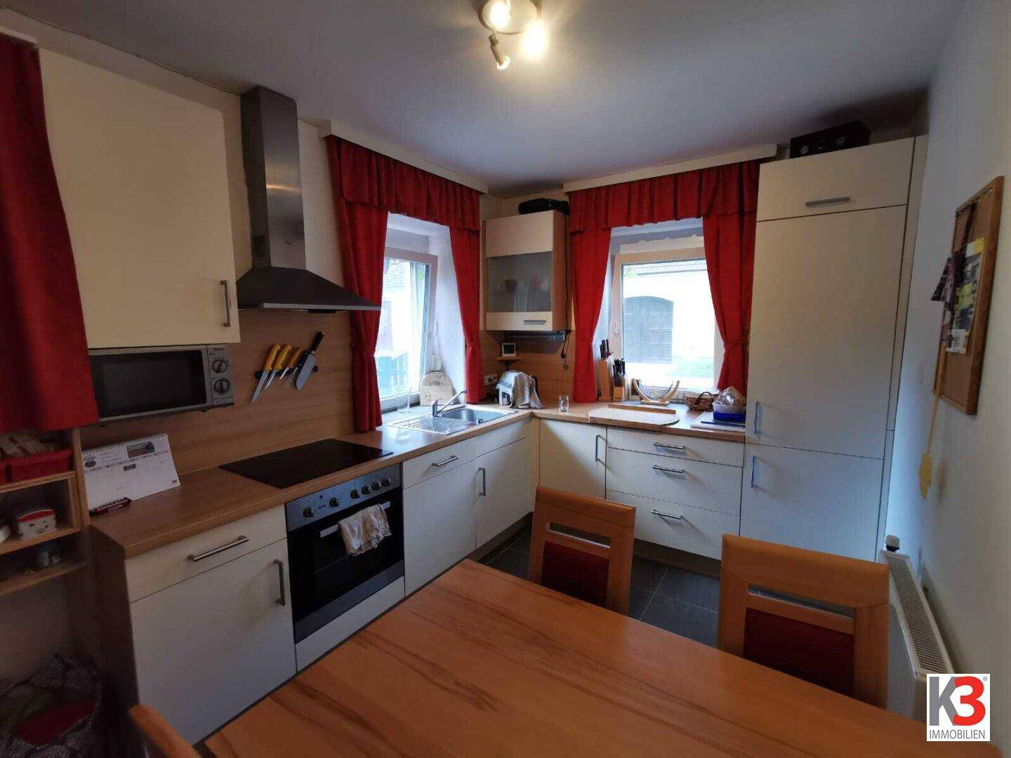 Die helle Küche mit Essbereich, modernen Geräten, Holztheke und roten Vorhängen.