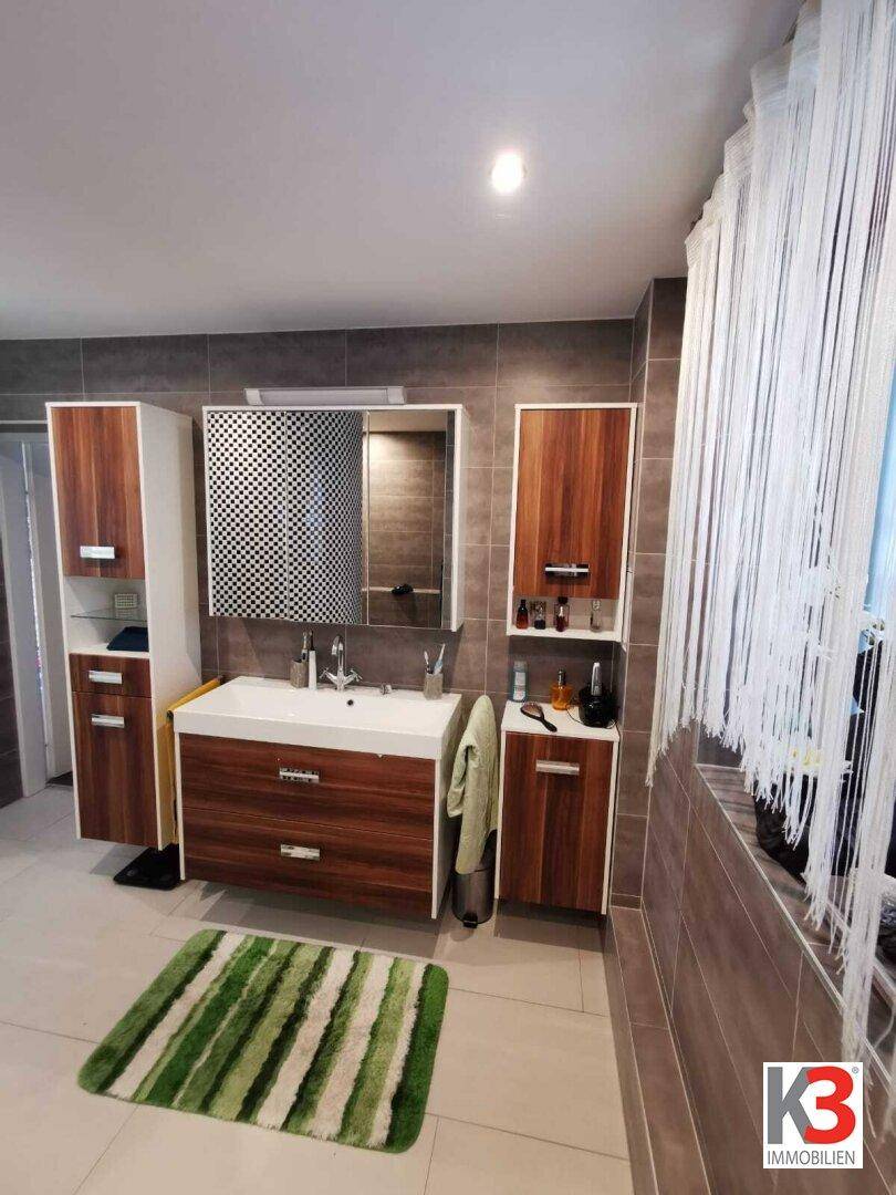 Das moderne Badezimmer mit Waschtisch, Spiegel, Holzmöbeln und grauen Fliesen.