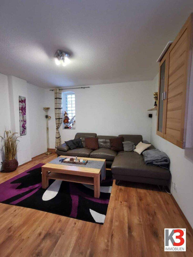 Das gemütliche Wohnzimmer mit braunem Ledersofa, Holzboden und farbenfrohem Teppich.