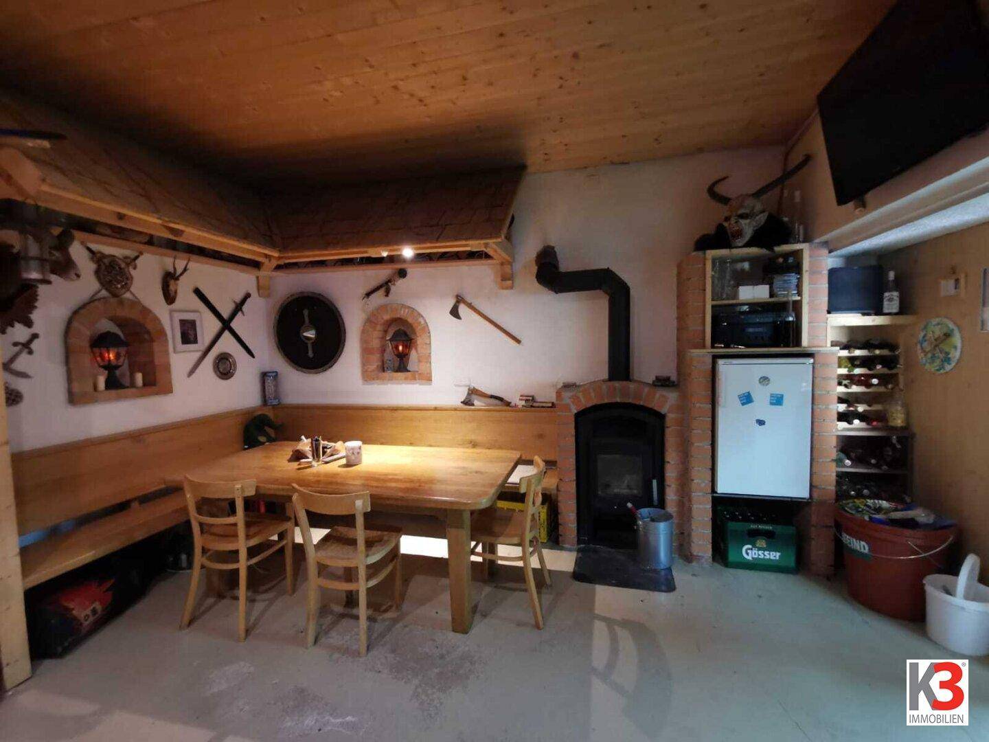 Das rustikale Esszimmer mit Kamin, Holztisch, Holzbalkendecke und Weinkühler.
