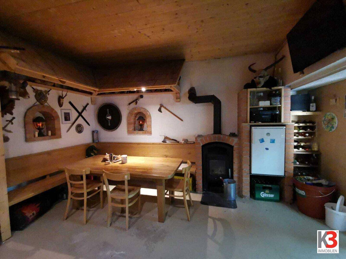Das rustikale Esszimmer mit Kamin, Holztisch, Holzbalkendecke und Weinkühler.