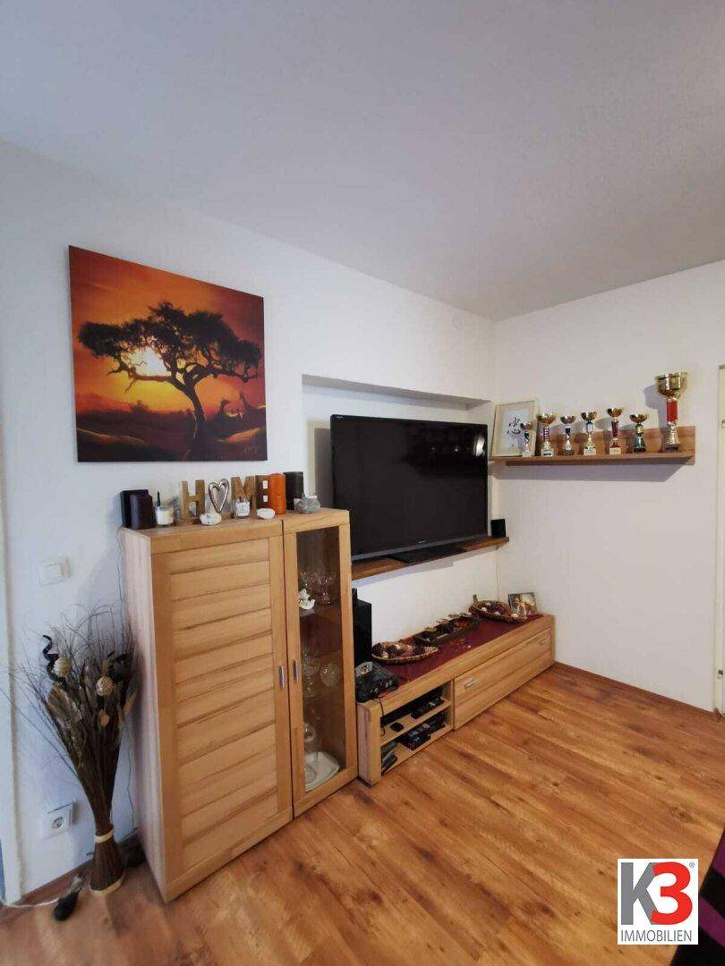 Das Wohnzimmer mit Fernseher, Holzmöbeln und einem dekorativen Wandbild.