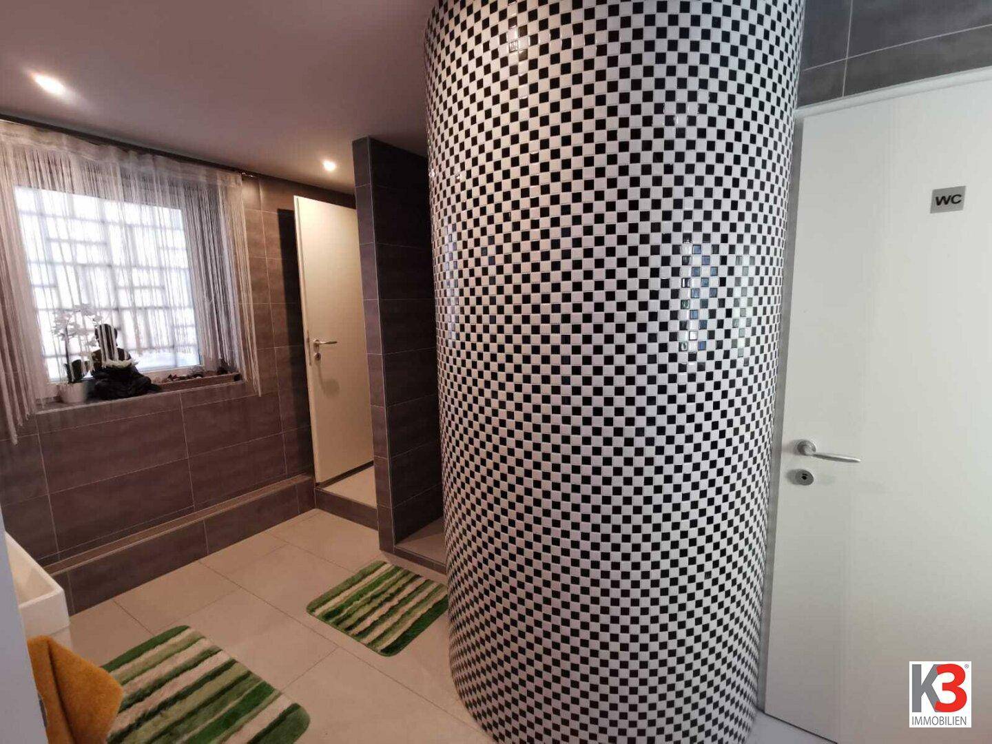 Das Badezimmer mit Duschbereich und einer dekorativen Säule mit Fliesenmuster.