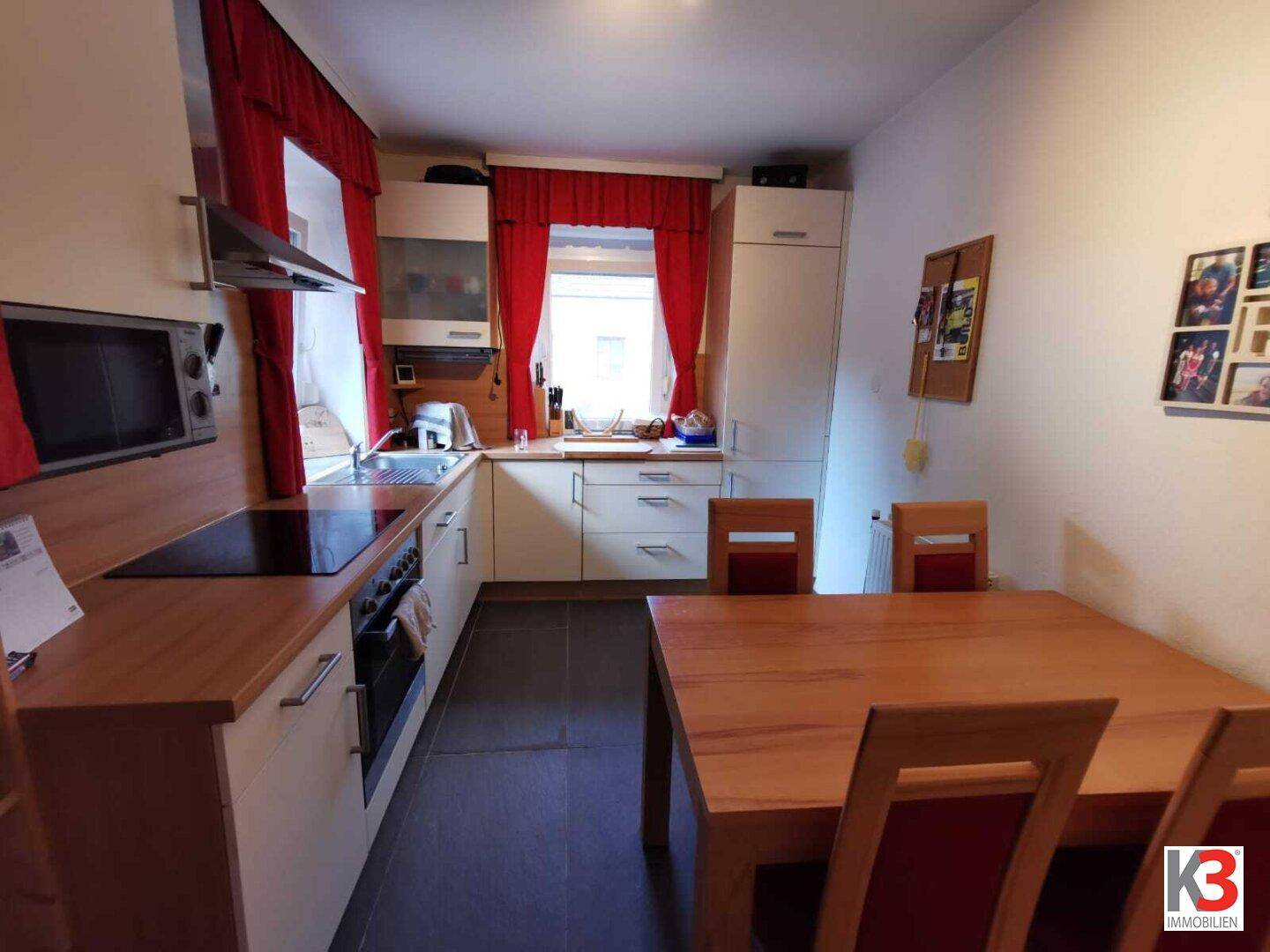 Die helle Küche mit Essbereich, modernen Geräten, Holztheke und roten Vorhängen.
