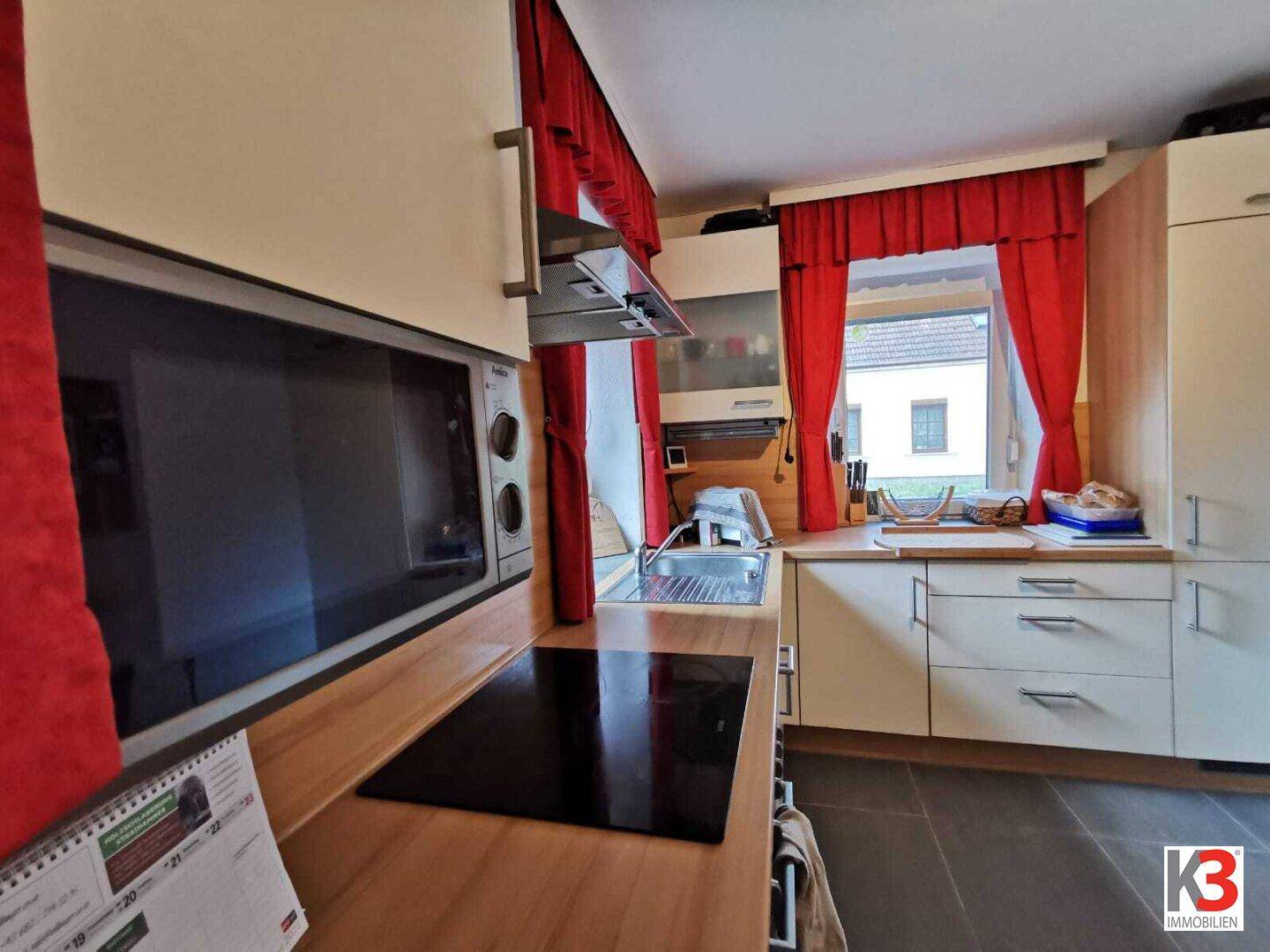 Die Küchenzeile mit Induktionskochfeld, Mikrowelle und Holztheke.