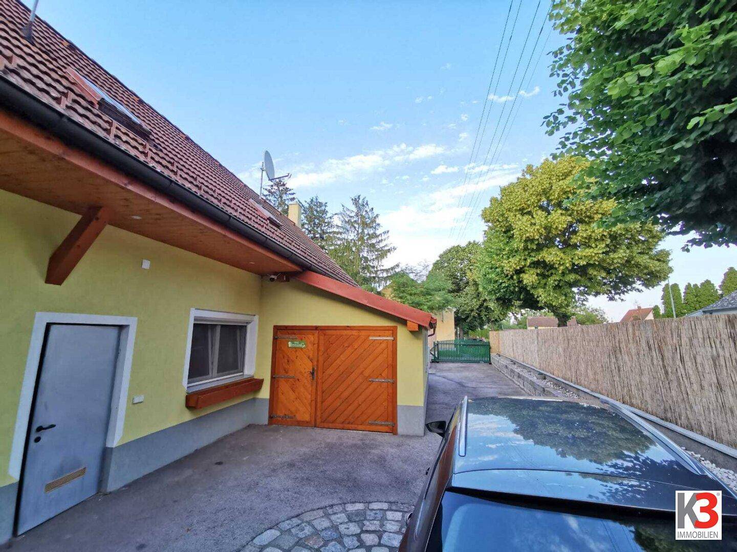 Die Seite des Hauses mit rustikalen Holztoren und einer gepflasterten Einfahrt.