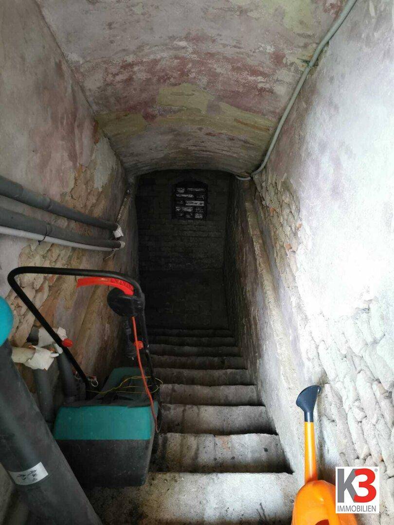 Eine Steintreppe, die in einen Keller mit unverputzten Wänden führt.