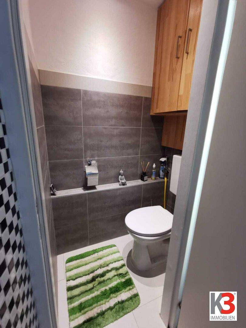 Das separate WC mit grauen Fliesen, Holzschränken und Wand-WC.
