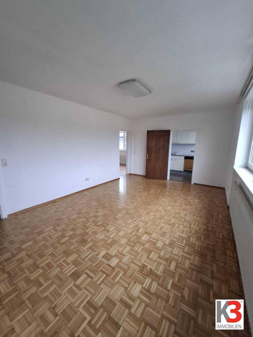 Helles Wohnzimmer mit klassischem Parkettboden und Zugang zu weiteren Räumen.
