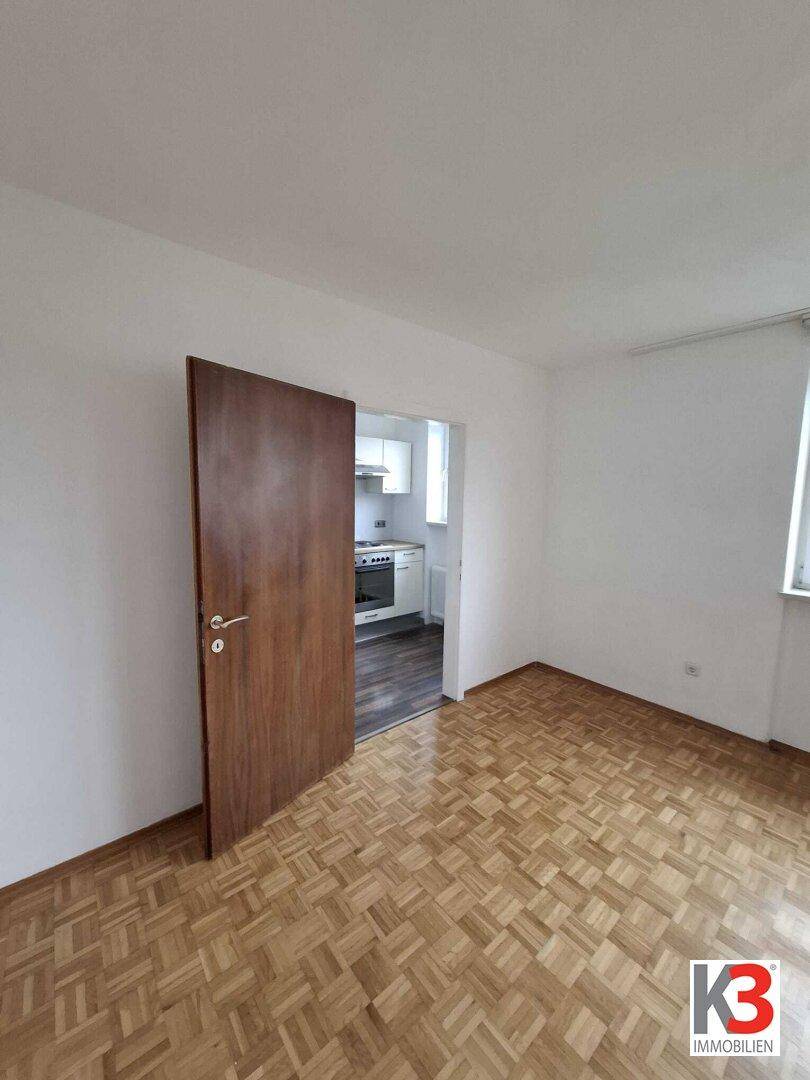 Geräumiger Wohnbereich mit Parkettboden und direktem Zugang zur Küche.