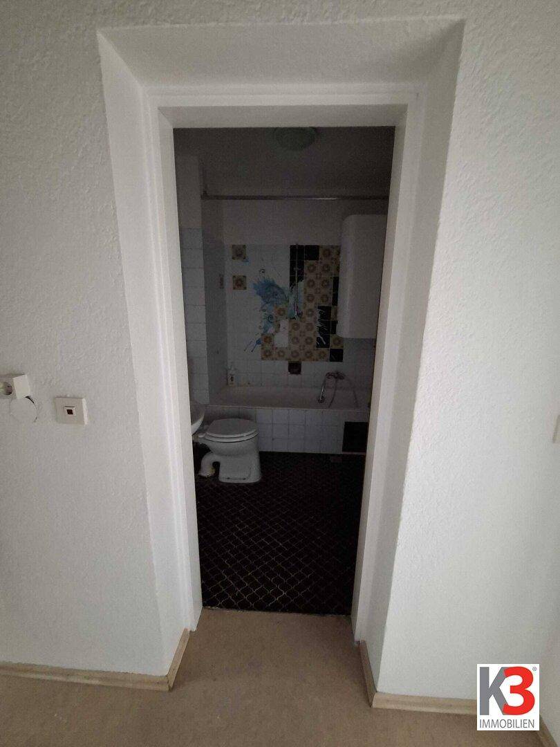 Badezimmer mit Badewanne, WC und dunklen Bodenfliesen im 80er-Jahre-Stil.
