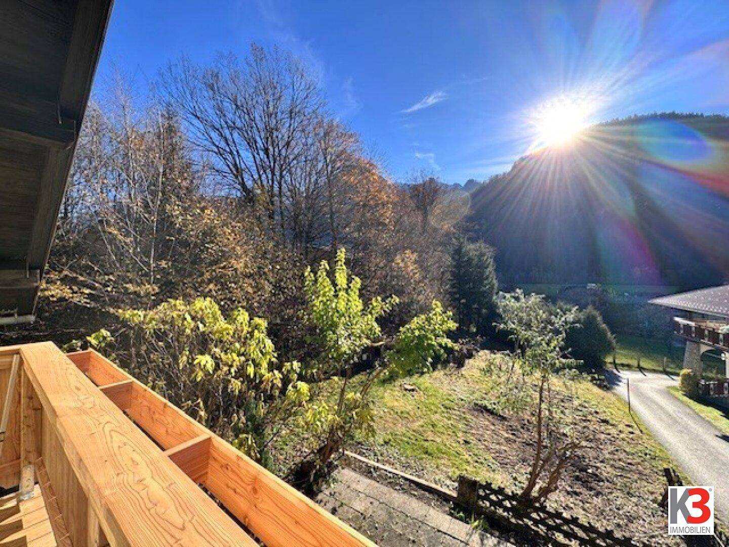 Sonniger Balkon mit Holzbalken und weitem Blick auf die bewaldeten Berge.