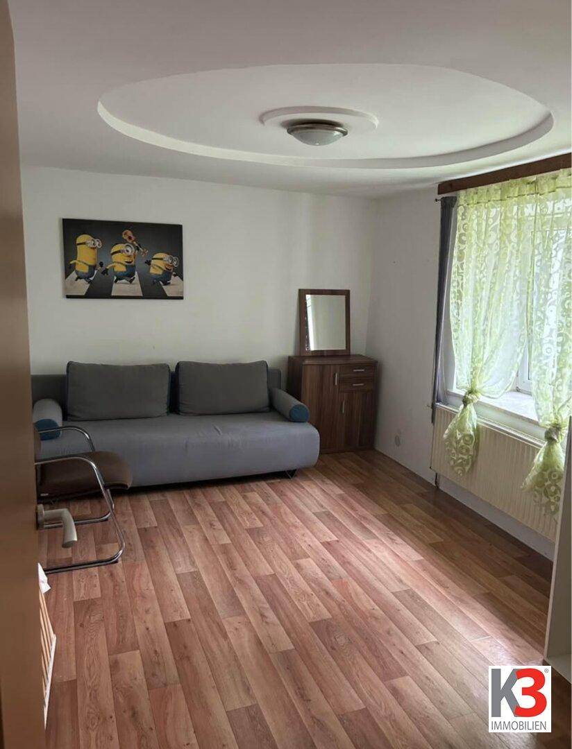 Helles Zimmer mit Sofa, Holzparkett und dekorativer Deckenbeleuchtung.