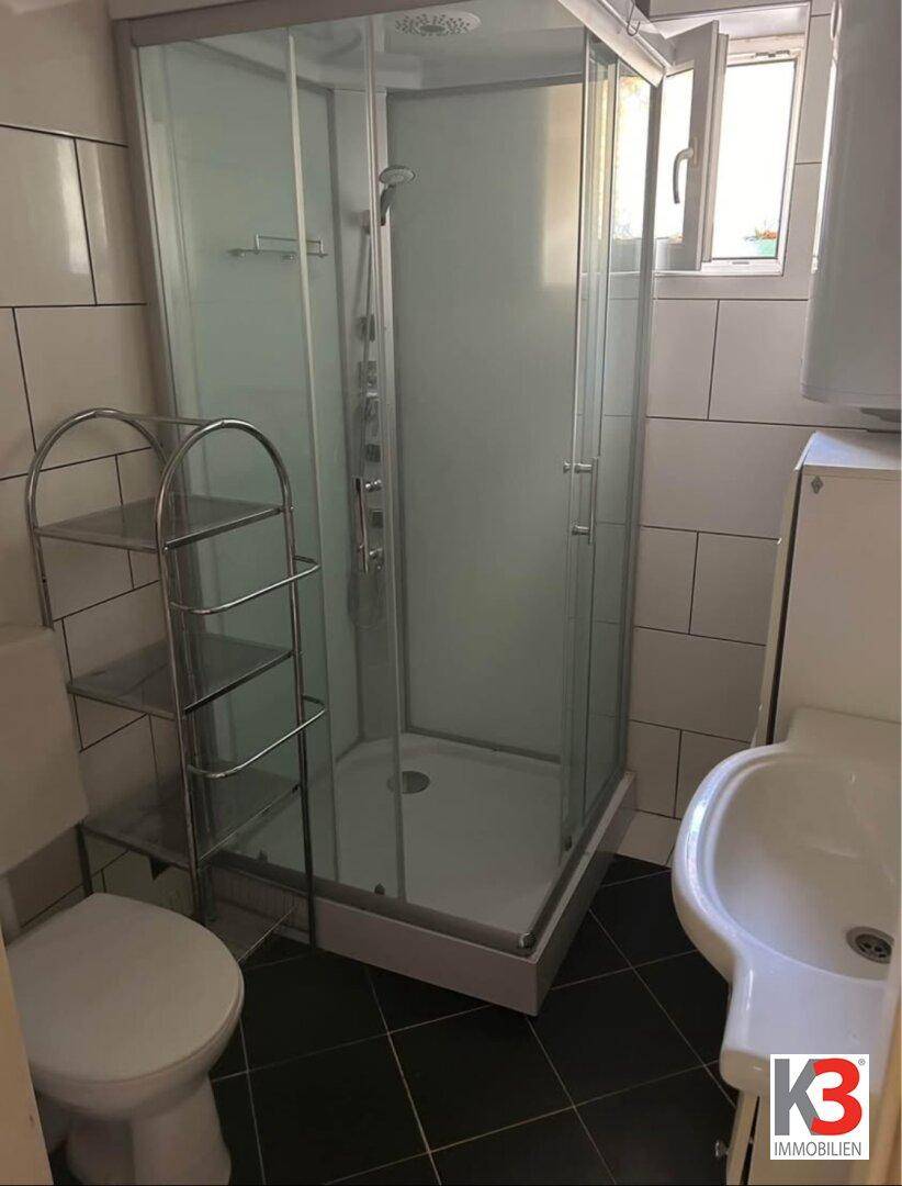 Kleines Badezimmer mit Duschkabine, WC und Fenster für Belüftung und Tageslicht.