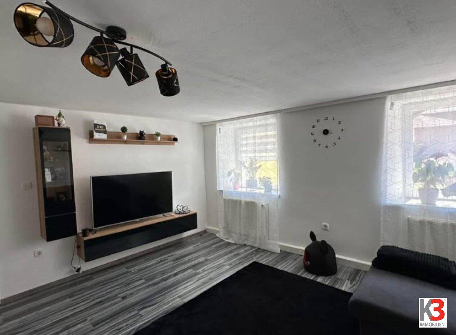 Heller Wohnbereich mit großem Fernseher, schwebenden Regalen und modernem Deckenlicht.
