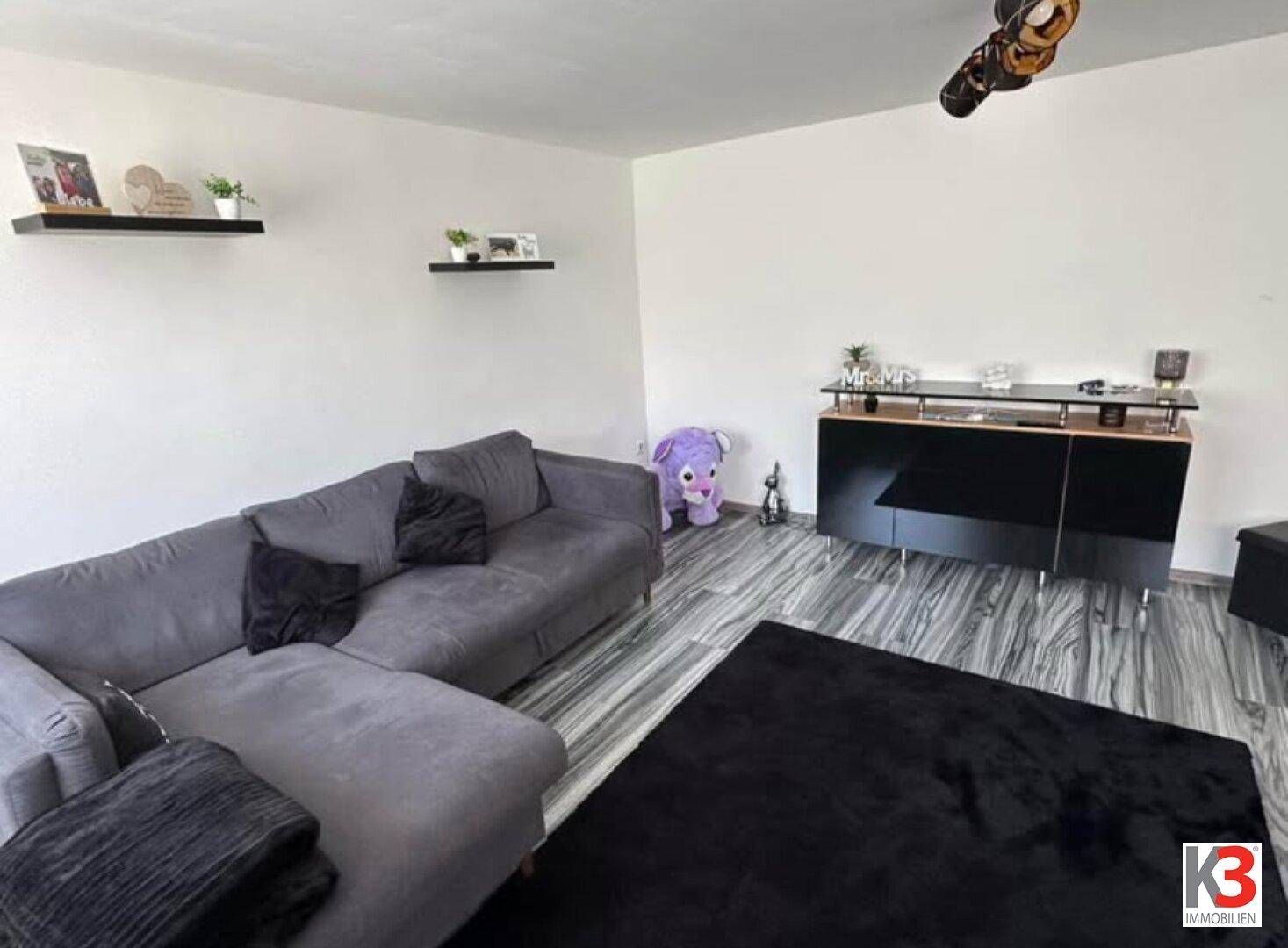 Geräumiges Wohnzimmer mit bequemer Eckcouch, dunklem Teppich und moderner Kommode.