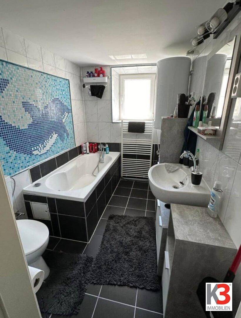 Modernes Badezimmer mit Badewanne, Mosaikfliesen und Fenster für Tageslicht.