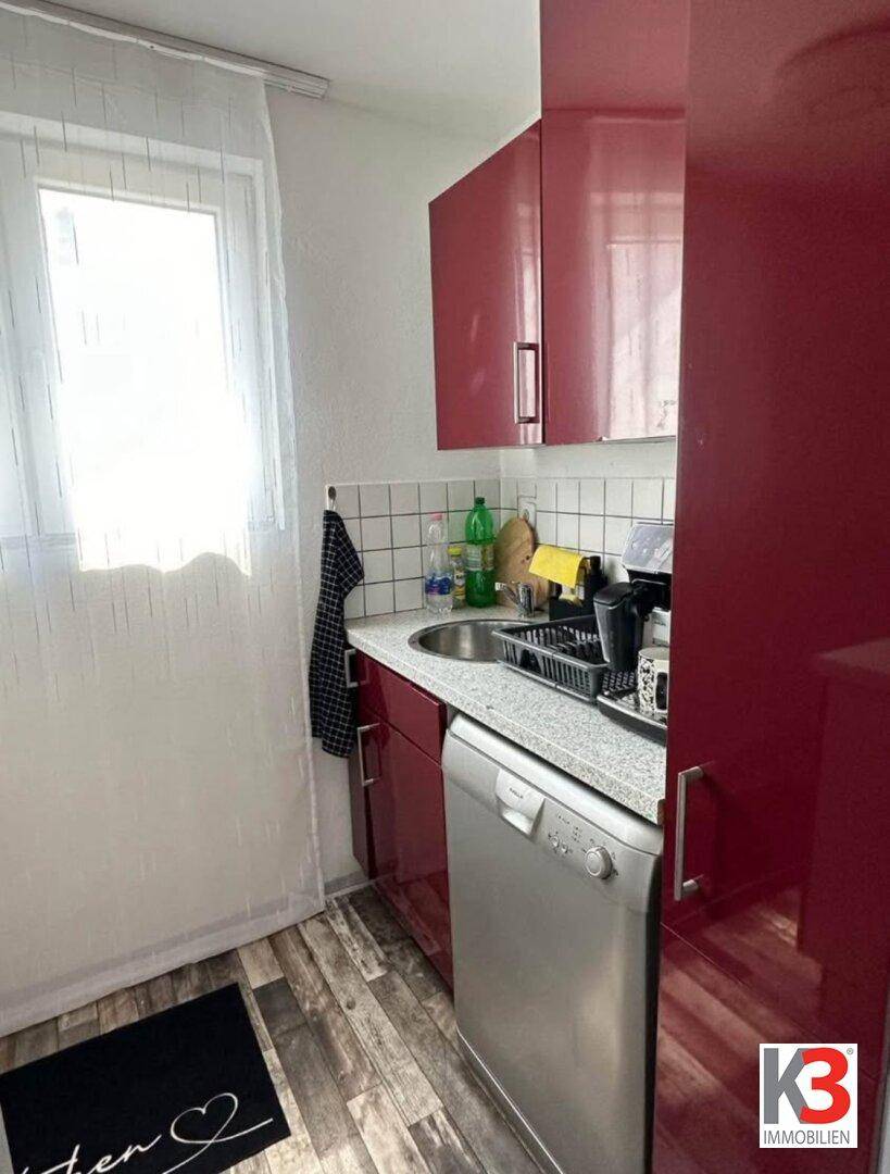 Kompakte Küche mit roten Hochglanzfronten, Spülmaschine und Fenster für natürliches Licht.