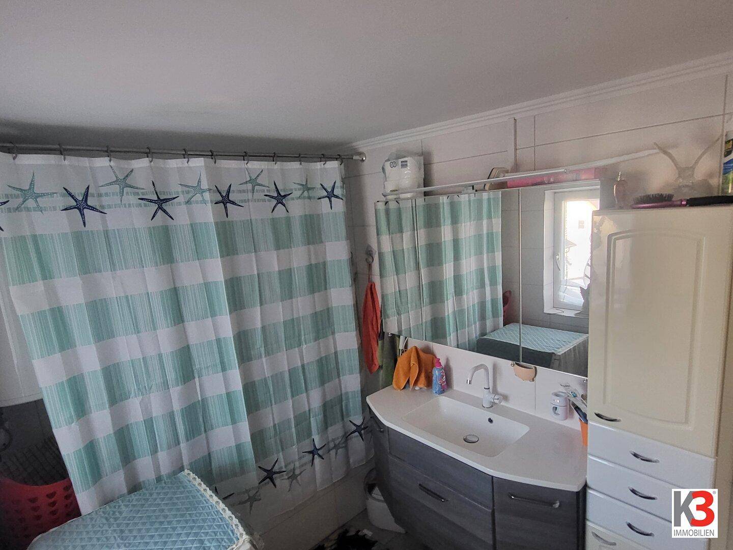 Helles Badezimmer mit Waschbecken, Spiegel und Fenster, dekoriert mit Duschvorhang.
