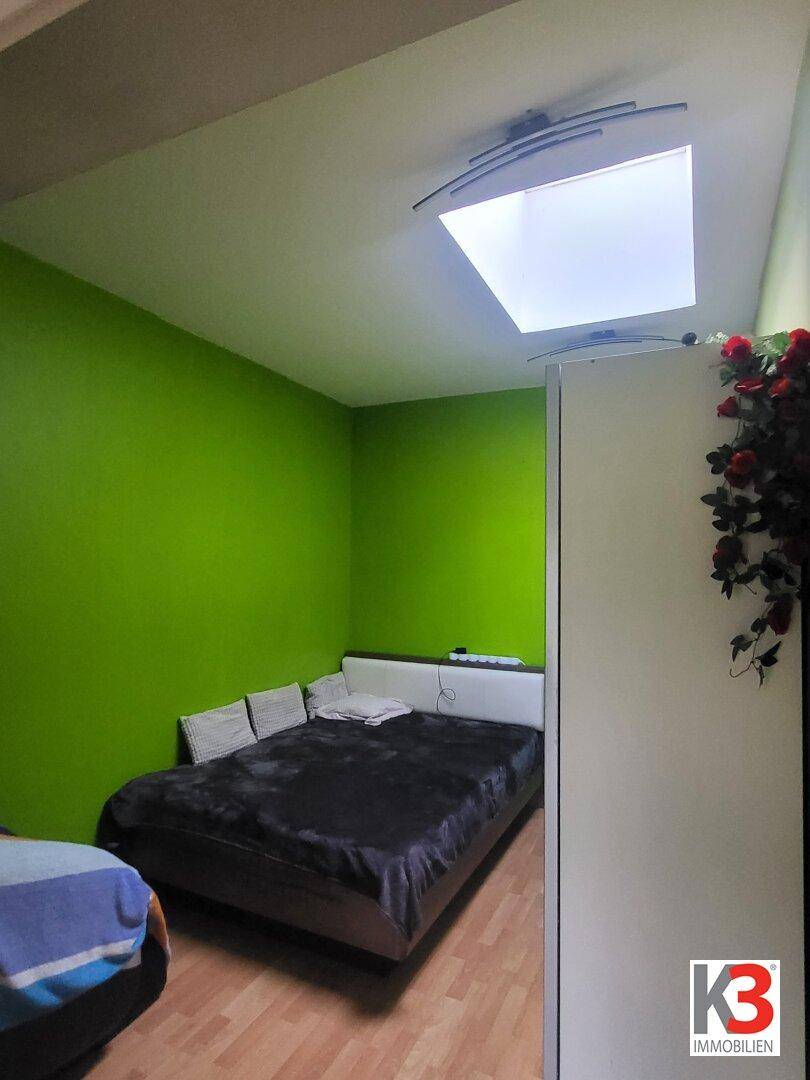 Schlafzimmer mit grünen Wänden, Doppelbett und Holzparkettboden.