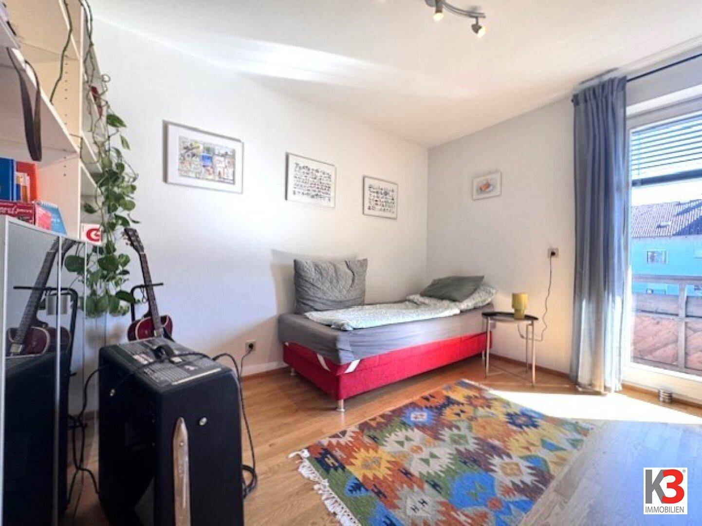 Helles Schlafzimmer mit Holzboden, Einzelbett und Zugang zu einem Balkon.