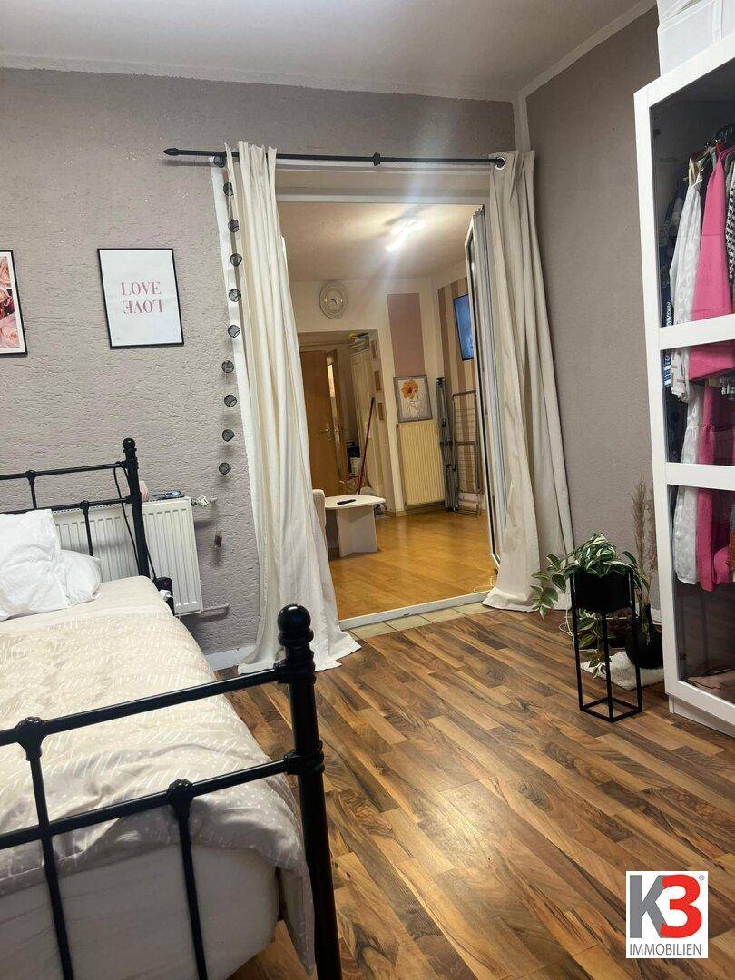 Schlafzimmer mit dunklem Holzbett, hellem Laminatboden und Zugang zu einem weiteren Raum.