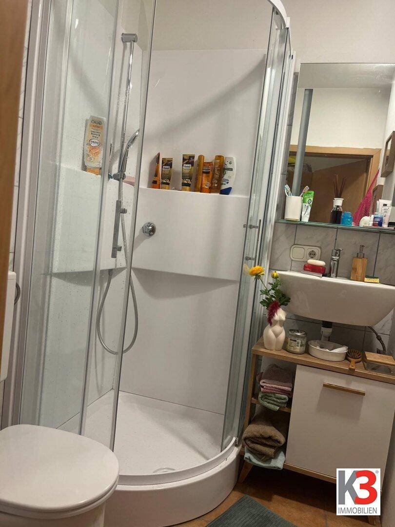 Modernes Badezimmer mit Duschkabine, Waschbecken und Spiegel, ausgestattet mit hellen Fliesen.