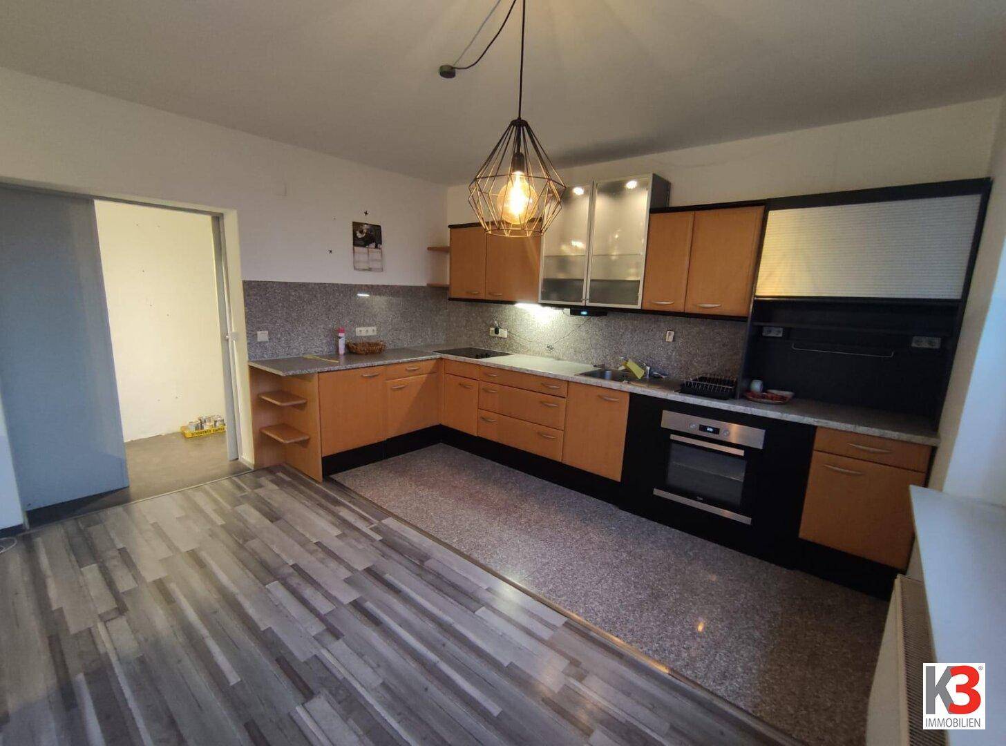 Funktionale Küche mit Holzschränken, Einbaugeräten und einem modernen Hängelampen-Design.