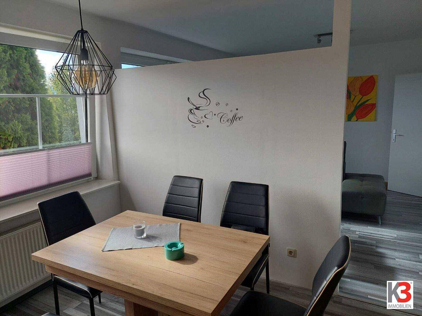 Essbereich mit Holztisch und schwarzen Stühlen, durch eine Wand vom Wohnbereich getrennt.