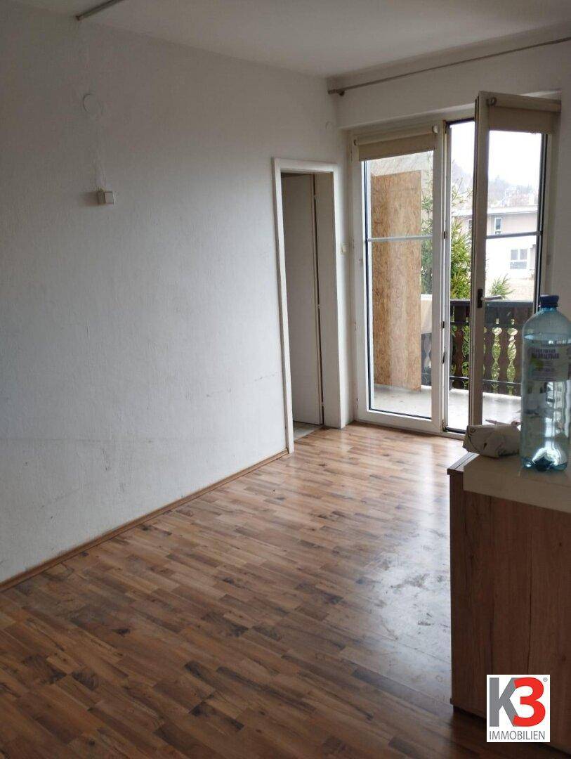 Leerer Raum mit Laminatboden und Zugang zu einem Balkon, der viel Tageslicht hereinlässt.