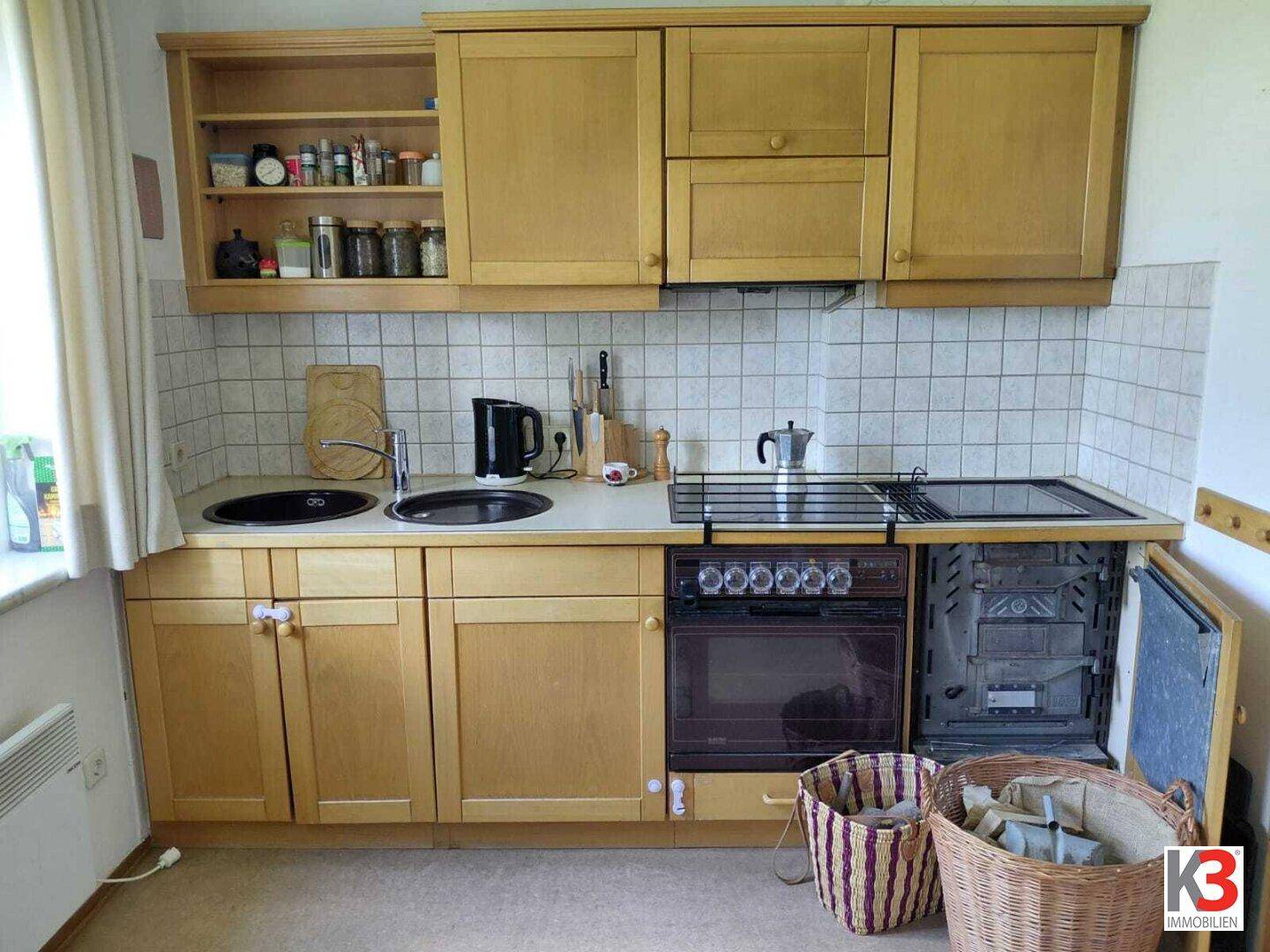 Einfache Küche mit hellen Holzschränken, gefliester Rückwand und integriertem Backofen.