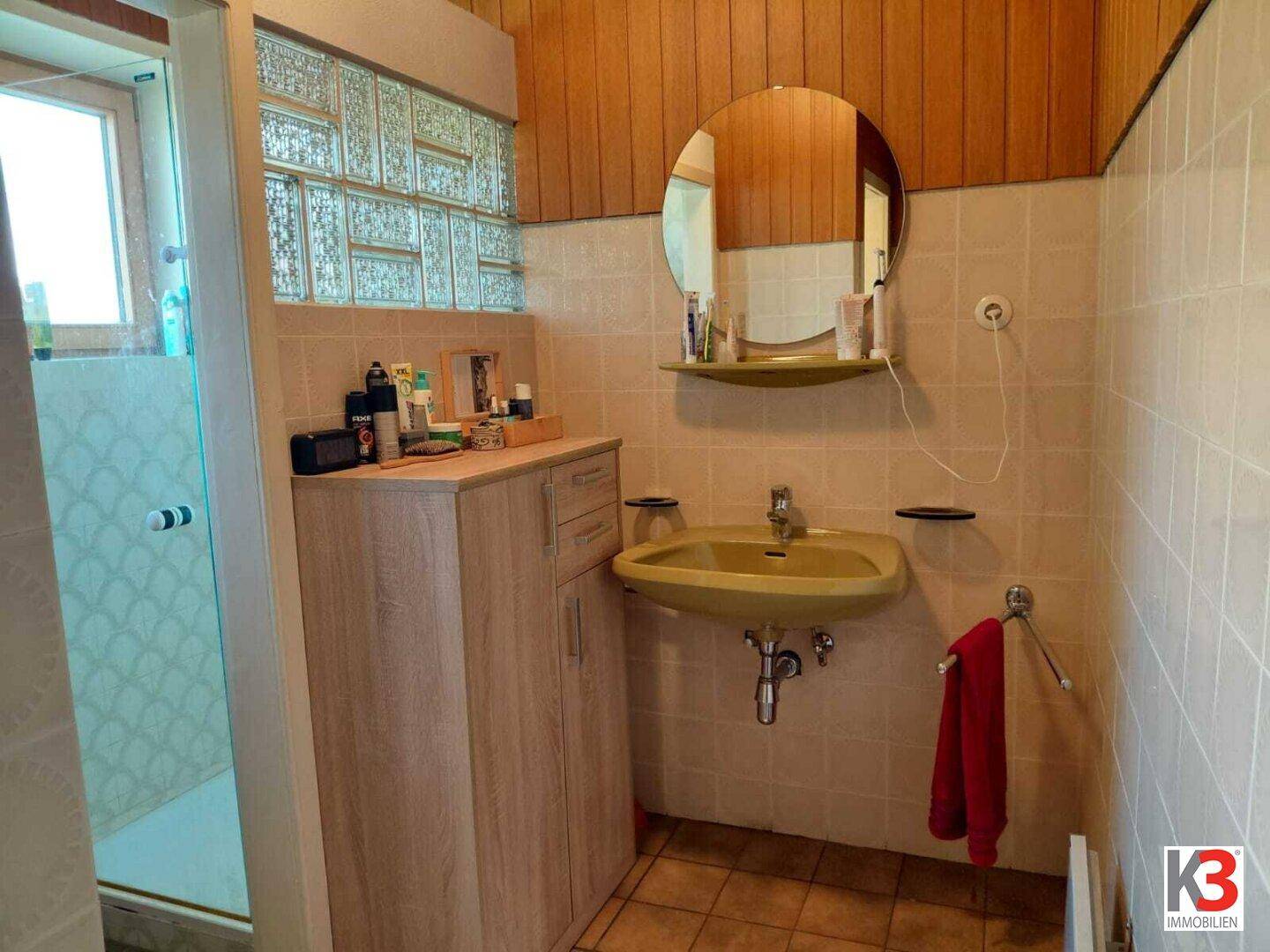 Badezimmer im 80er-Jahre-Stil mit gelbem Waschbecken, Duschkabine und Holzverkleidung an der Wand.