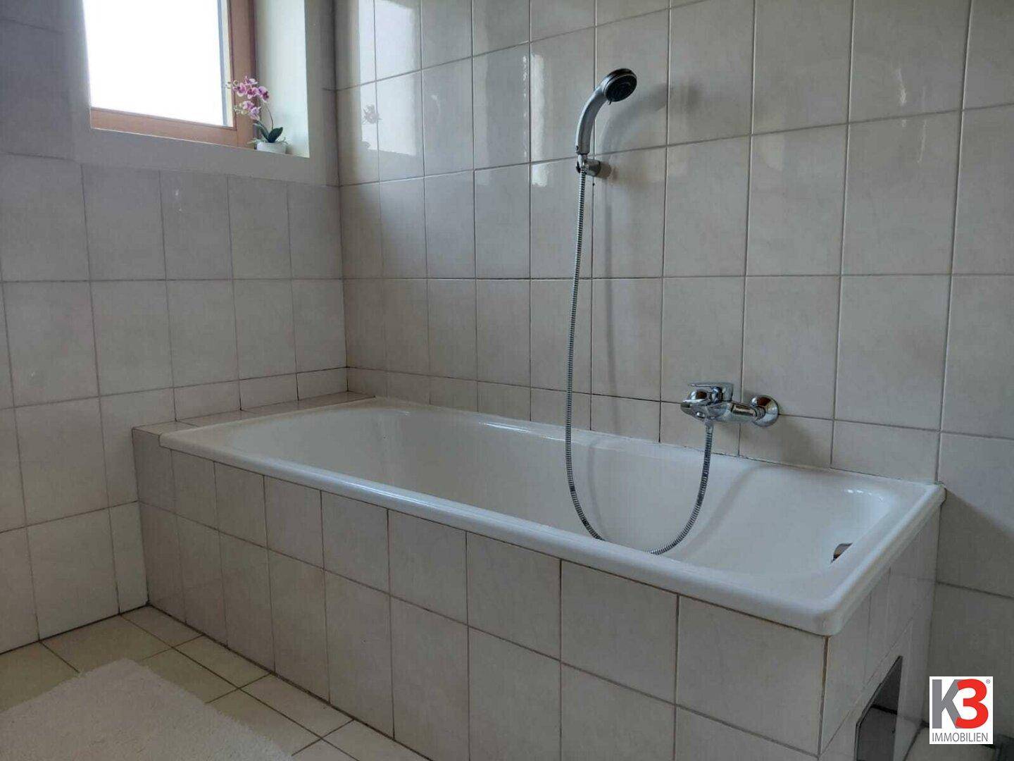 Badezimmer mit eingebauter Badewanne und weißen Fliesen an Wänden und Boden.
