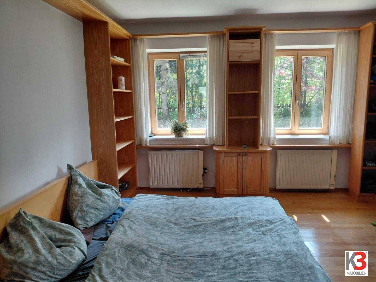 Schlafzimmer mit Doppelbett, Holzeinbauschränken und Blick ins Grüne durch große Fenster.