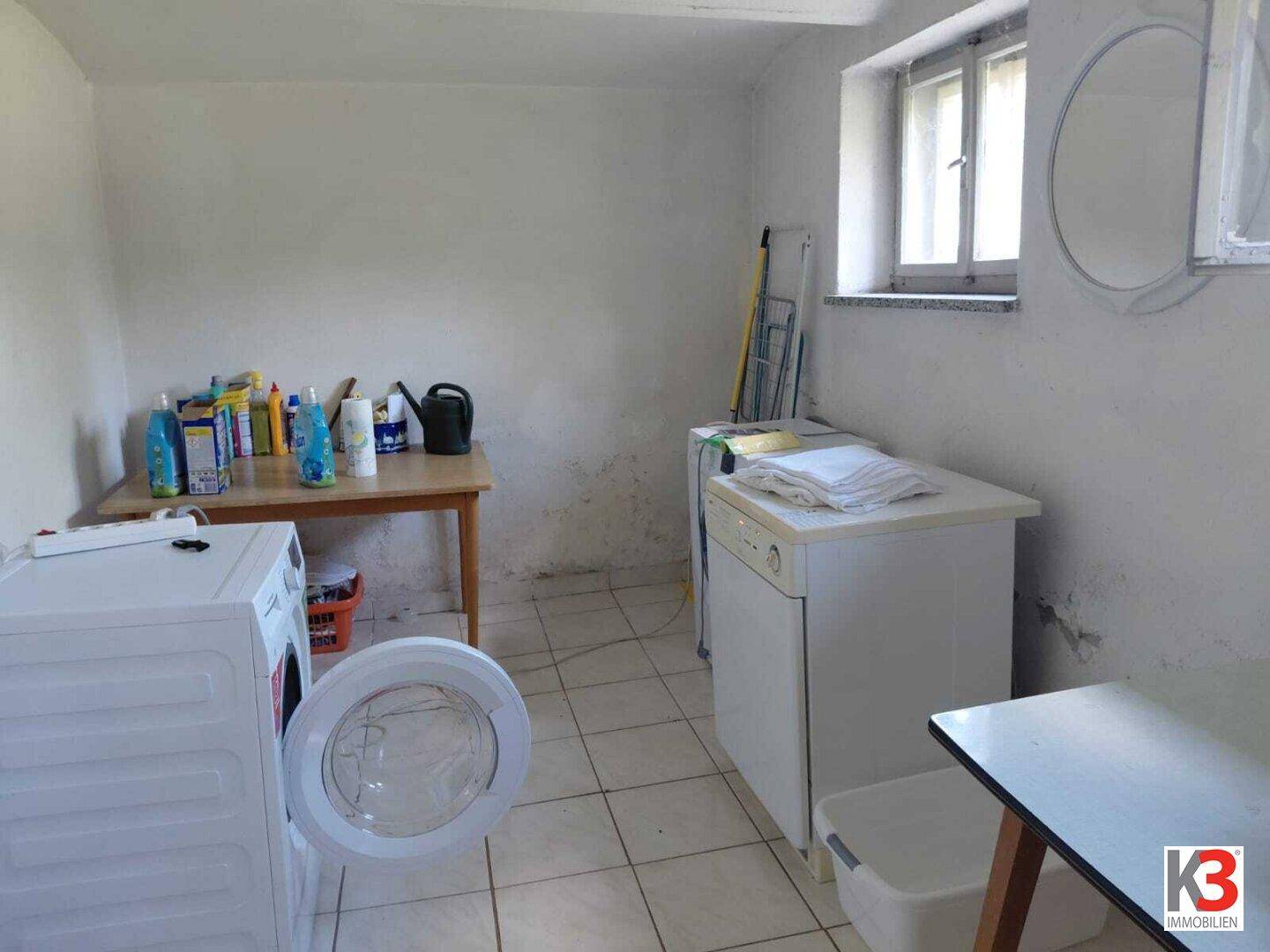 Waschküche im Keller mit Waschmaschine, Trockner und Fenster, ideal als Hauswirtschaftsraum.