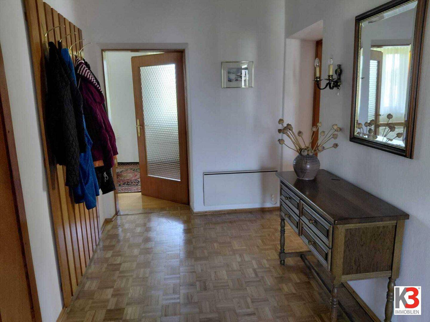 Heller Flur mit Parkettboden, Garderobe und antiker Kommode mit Spiegel.