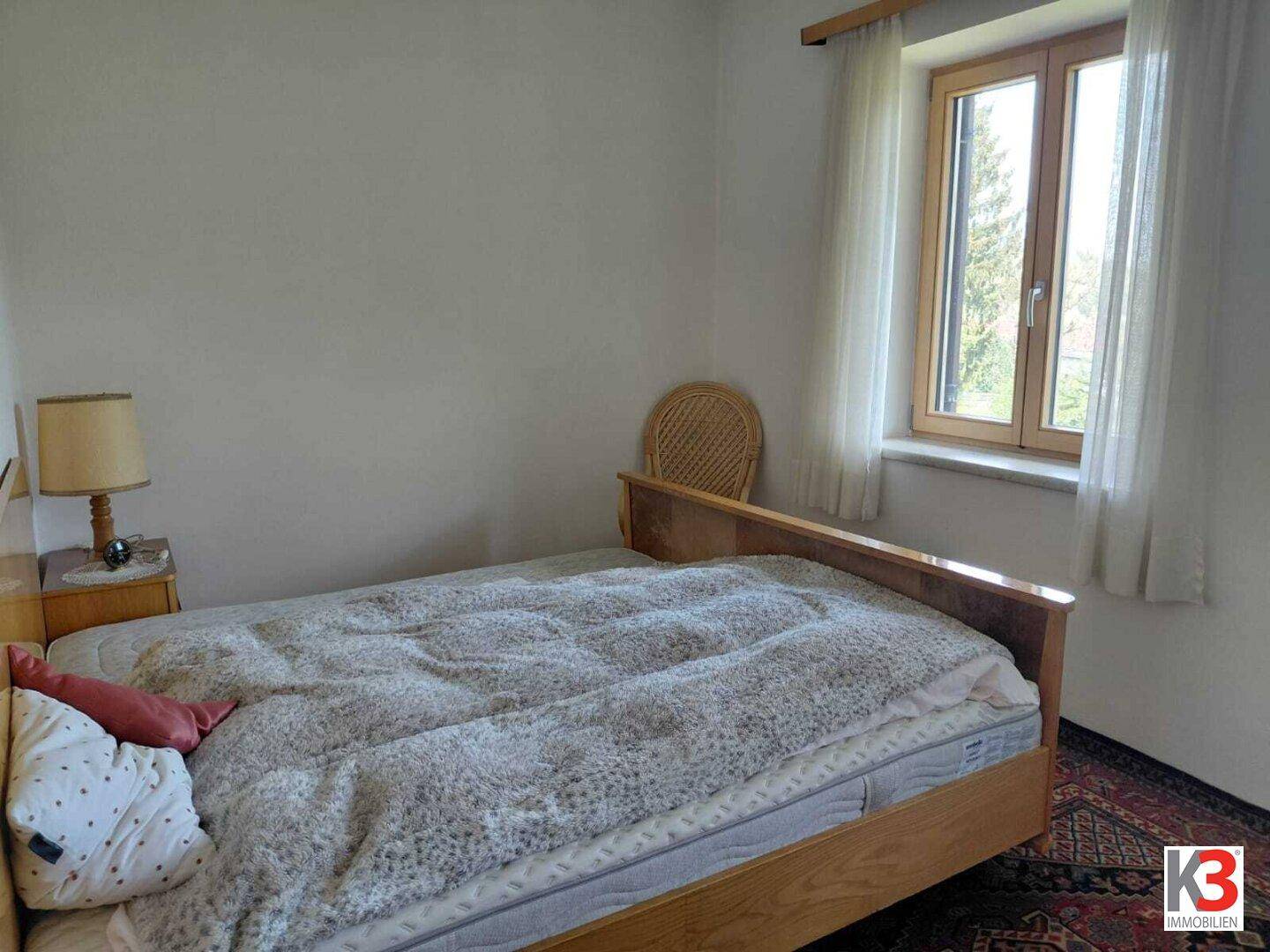 Schlafzimmer mit Einzelbett, Nachttischlampe und Fenster mit Blick ins Grüne.