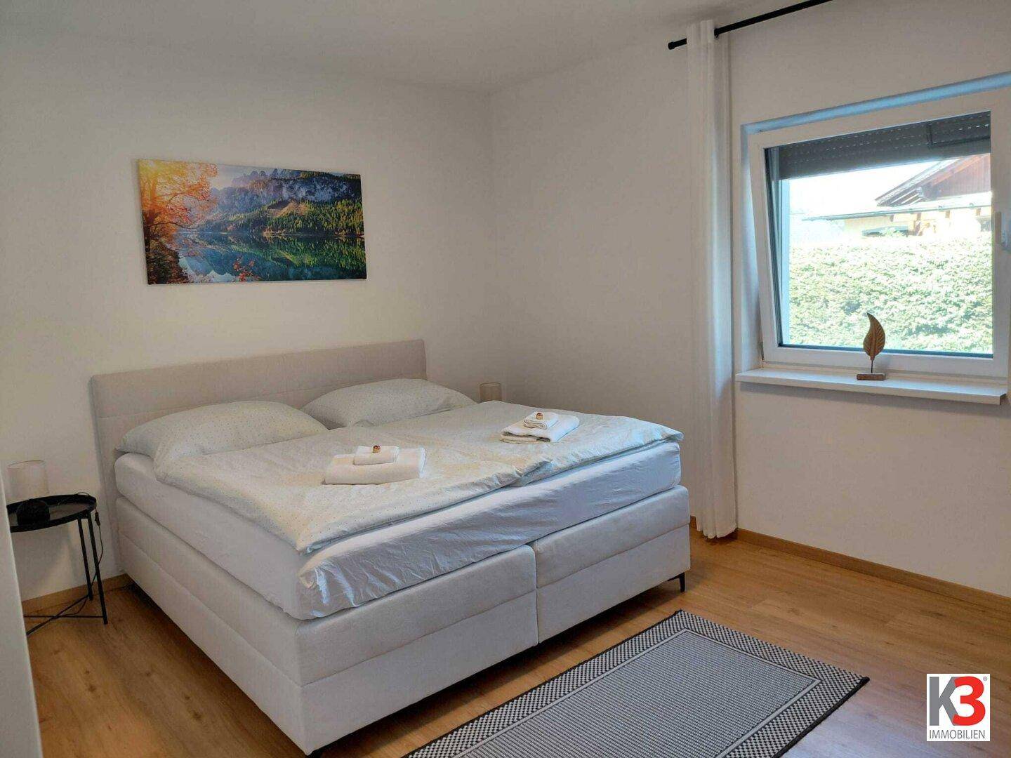 Schlafzimmer mit Doppelbett, Holzboden und einem Fenster mit Blick auf die Umgebung.