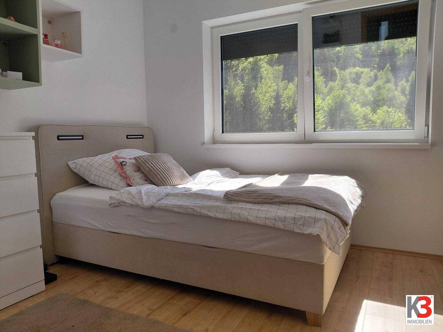 Helles Schlafzimmer mit Einzelbett, Holzboden und Blick ins Grüne.