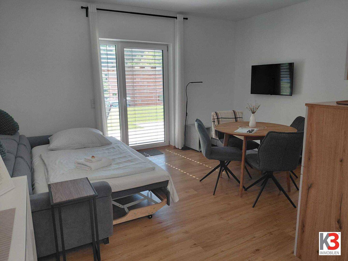 Wohnbereich mit Schlafsofa, Esstisch und Zugang zum Garten durch eine große Glastür.