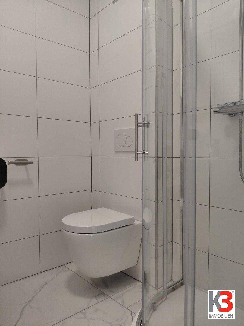 Kleines Badezimmer mit Duschkabine, Wand-WC und weißen Fliesen.