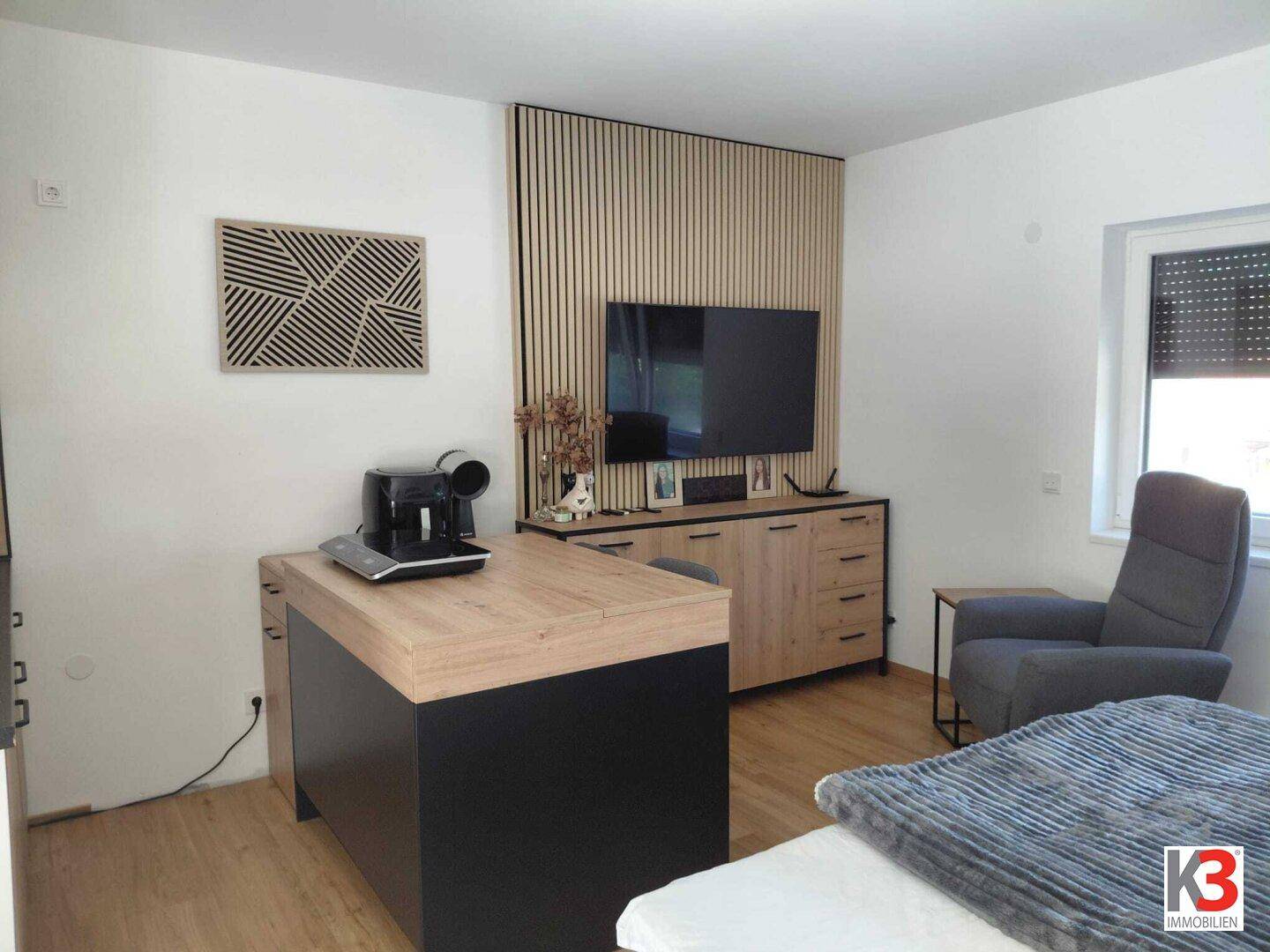 Multifunktionaler Wohnbereich mit Holzboden, TV-Wand und Kaffeemaschine.
