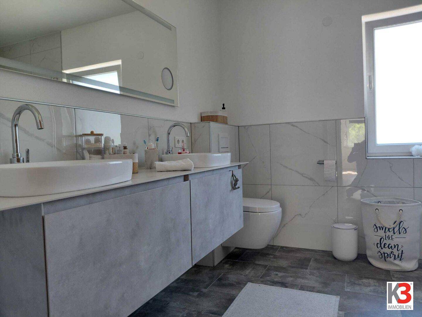 Modernes Badezimmer mit Doppelwaschbecken, Wand-WC und großformatigen Fliesen.