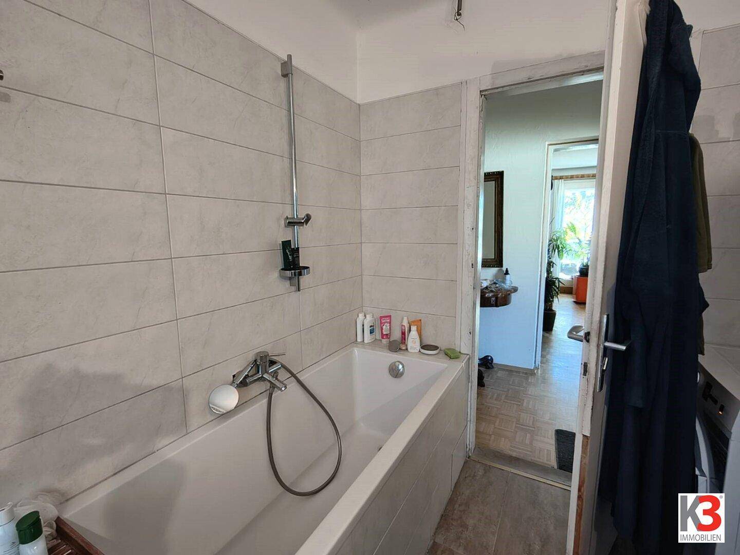 Badezimmer mit Badewanne, hellen Fliesen an den Wänden und Duschvorrichtung, in gutem Zustand.