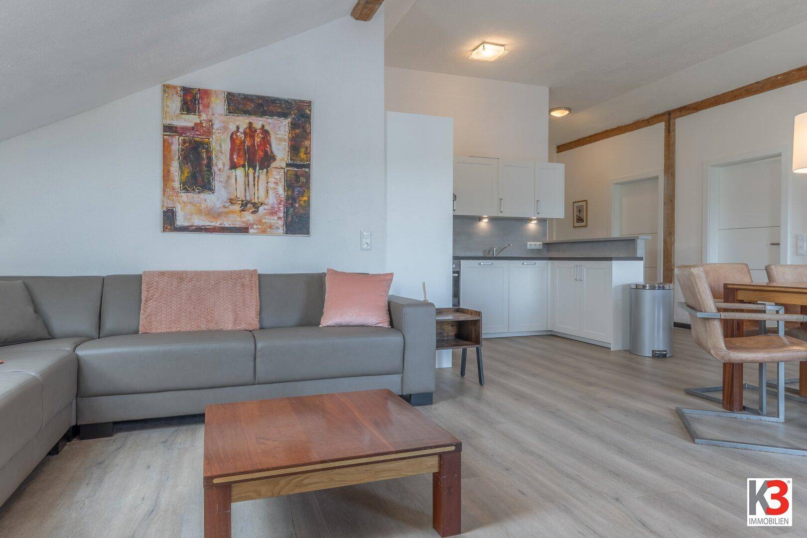 Gemütlicher Wohnbereich mit Sofa, Couchtisch und angrenzender Küchenzeile unter sichtbaren Holzbalken.