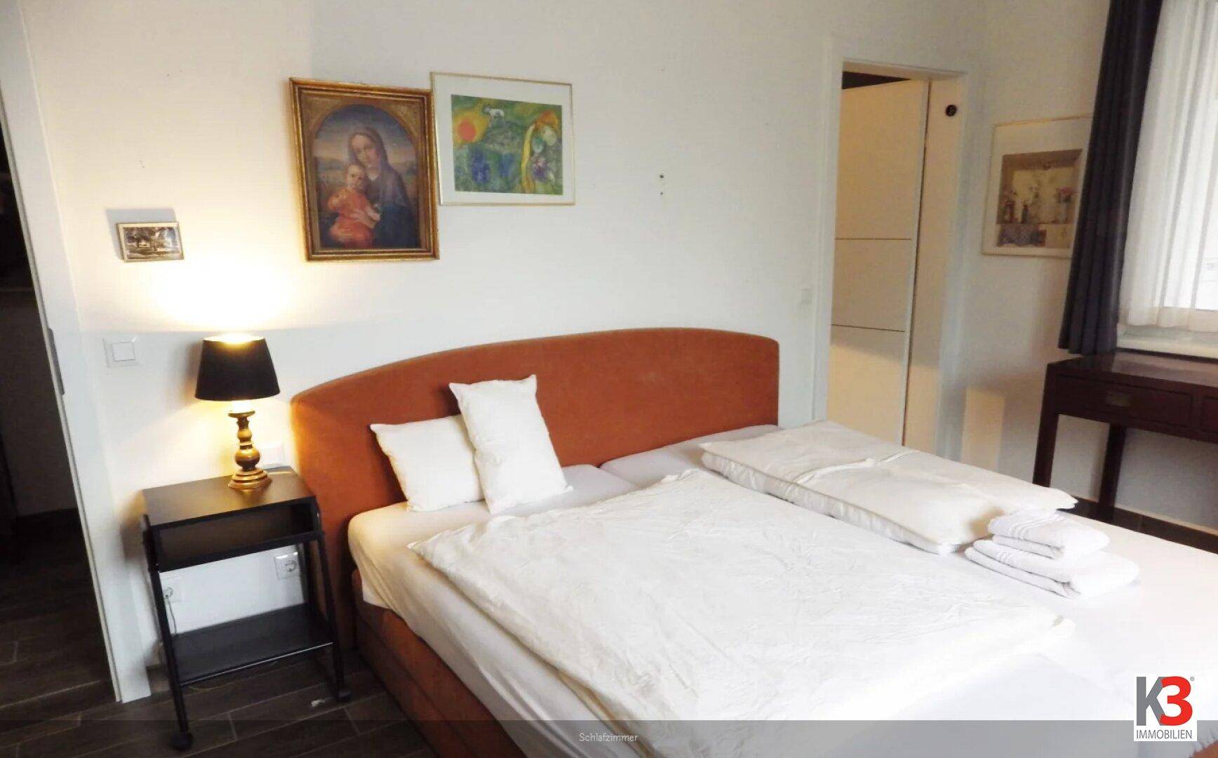Gemütliches Schlafzimmer mit Doppelbett, Nachttisch und Kunstwerken an der Wand.