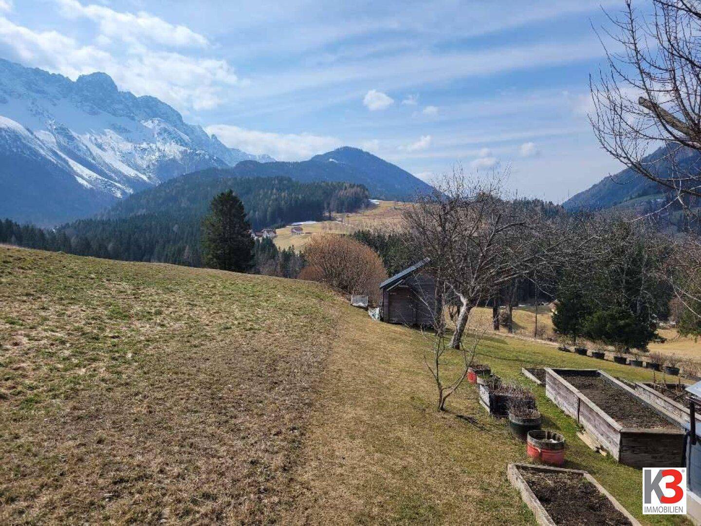 Großer Gartenbereich mit Hochbeeten und Panoramablick auf die majestätische Bergwelt.