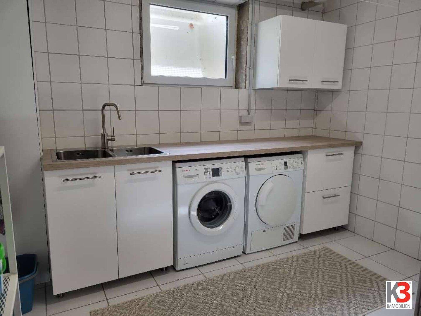Praktischer Hauswirtschaftsraum mit Waschmaschine, Trockner und Spülbecken.