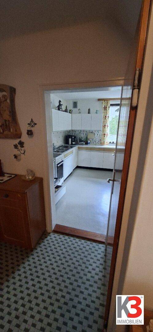 Blick vom Flur in eine Küche mit weißen Einbauschränken und einem Fenster.